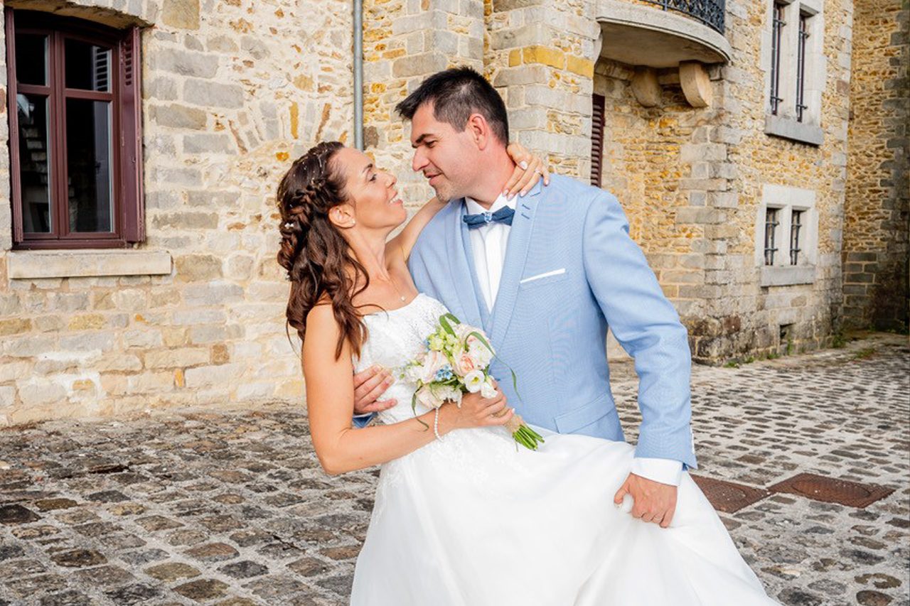 Mariés posant avec complicité devant une bâtisse en pierre, photographiés par Déborah Bernard